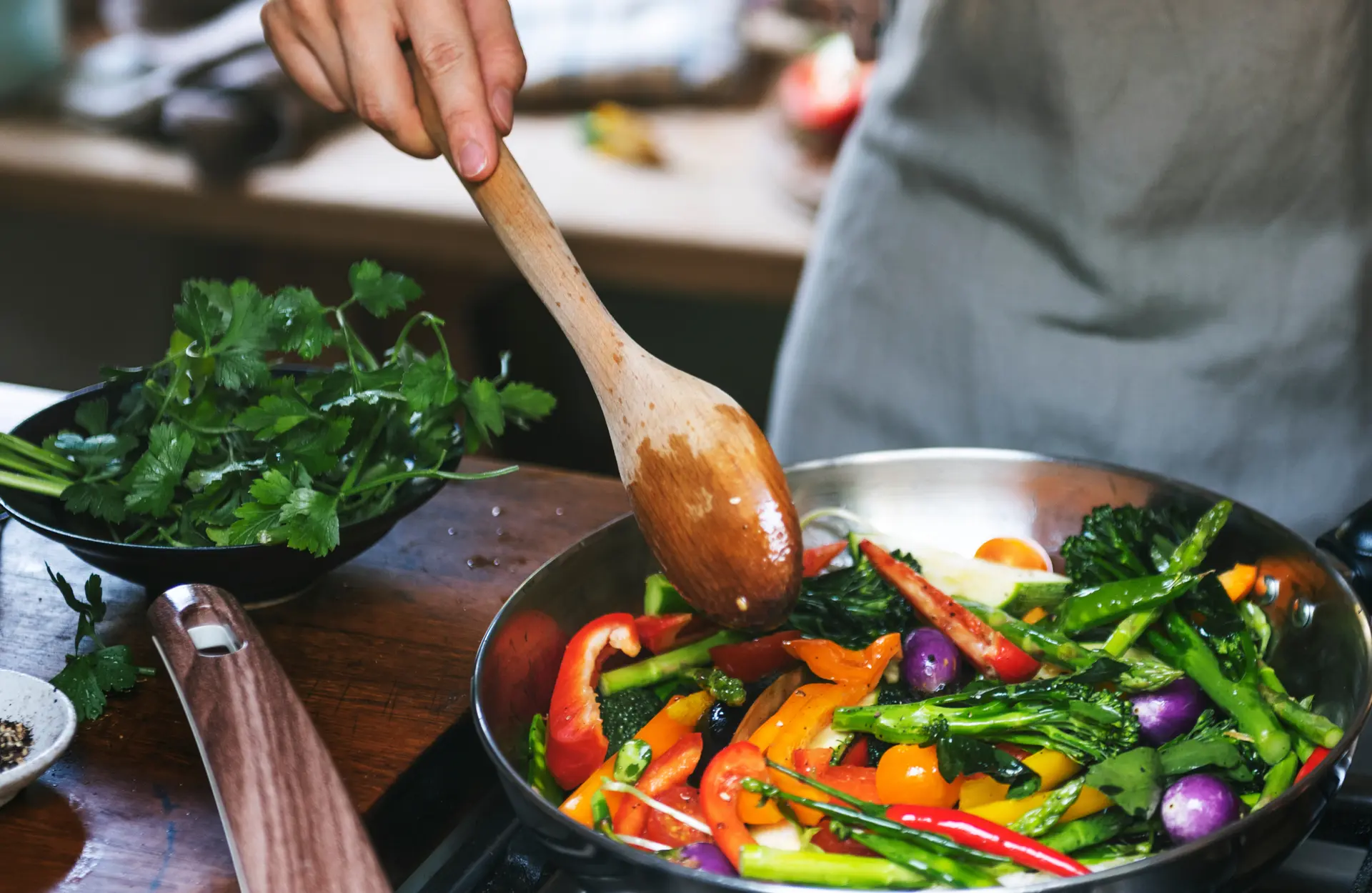 Sizzling vegetables in a frying pan, expertly stirred with a wooden spoon.