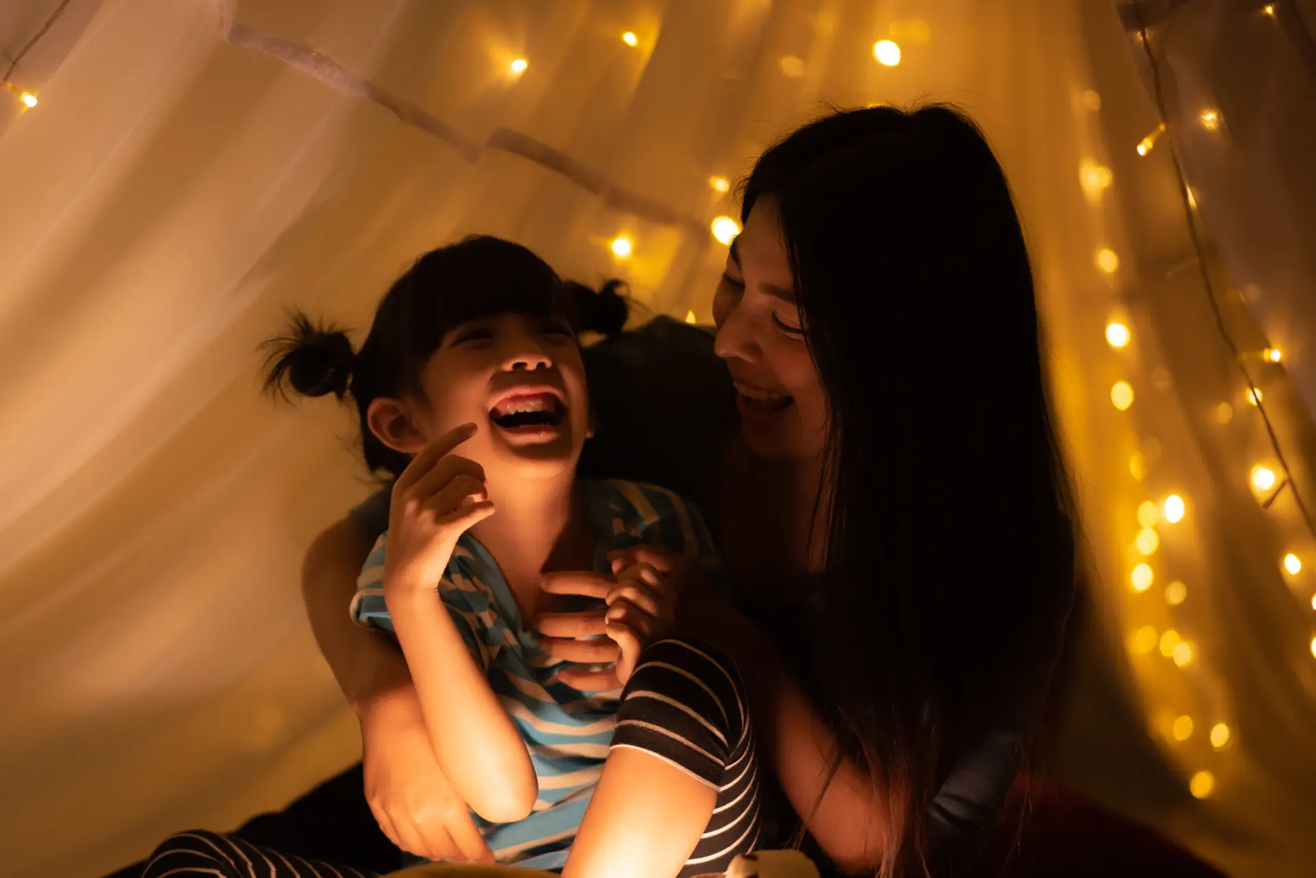 Joyful mother sharing a bedtime story, evoking laughter from her delighted daughter.